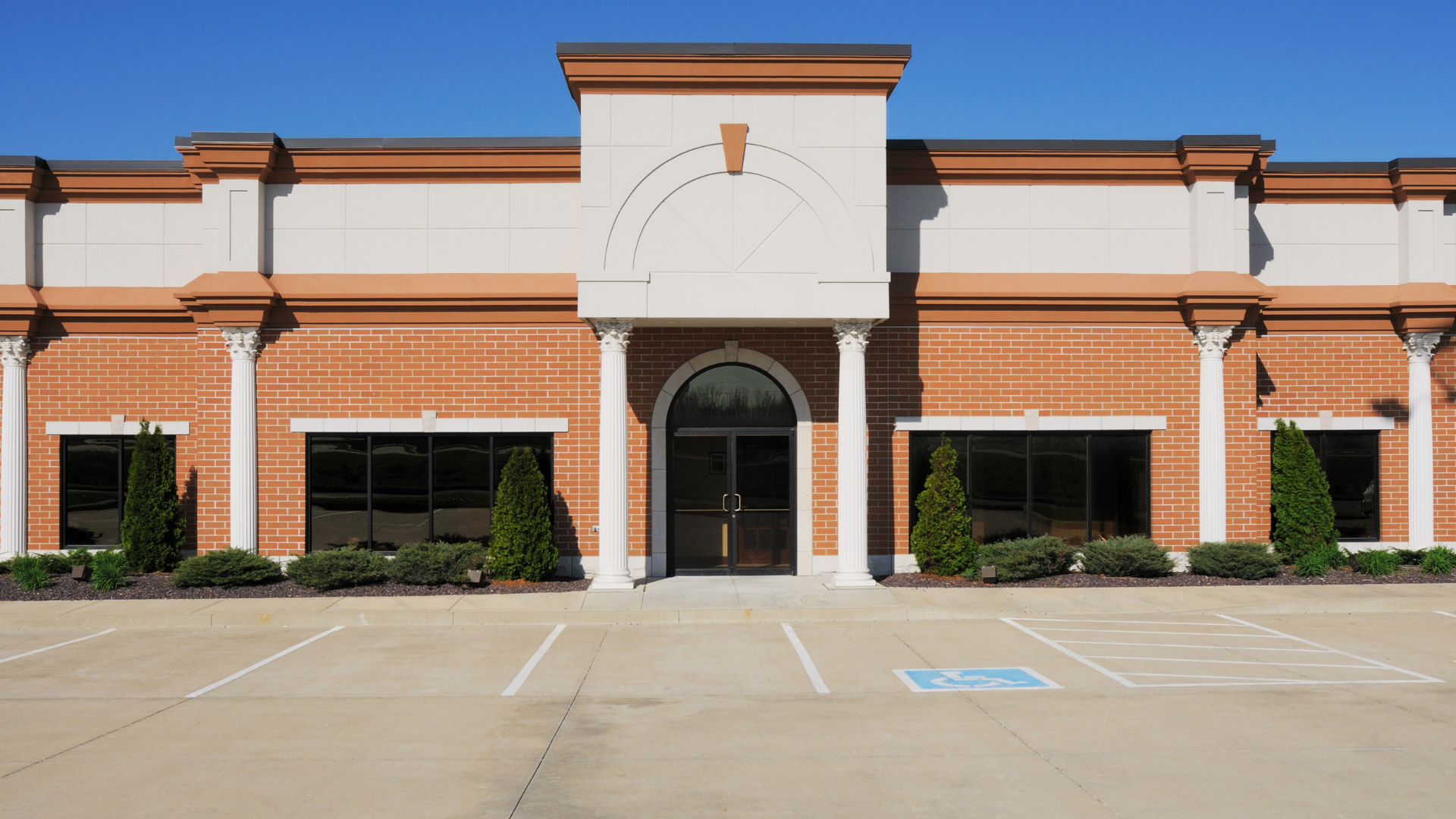 Front entrance of a brick commercial building with arched doorway and empty parking lot