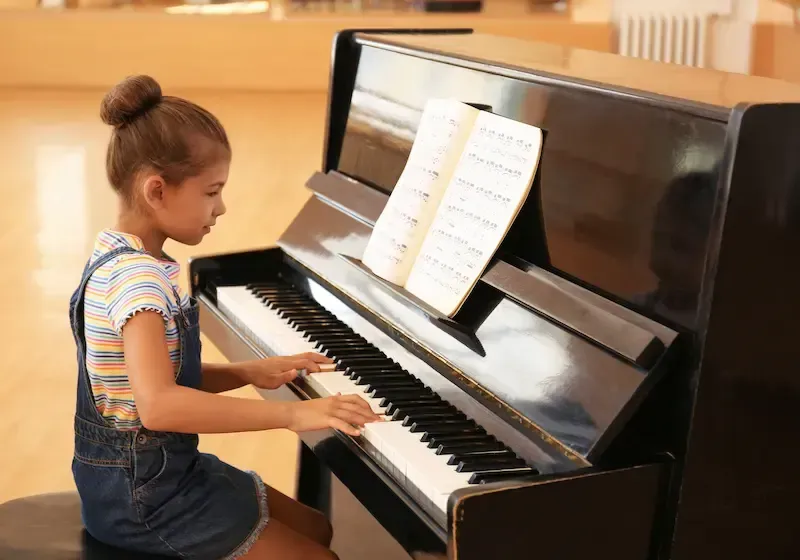 A child playing a piano with sheet music in a bright room.