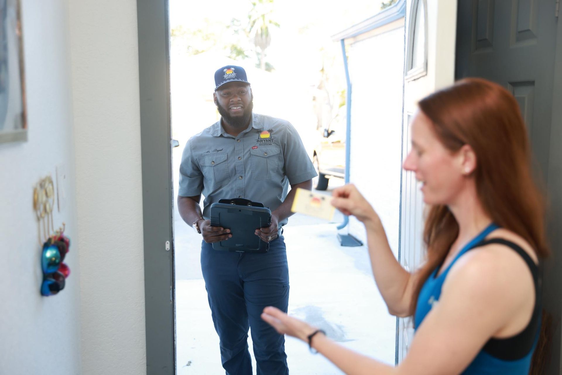 Delivery driver at a doorway handing a package to a woman in a blue top