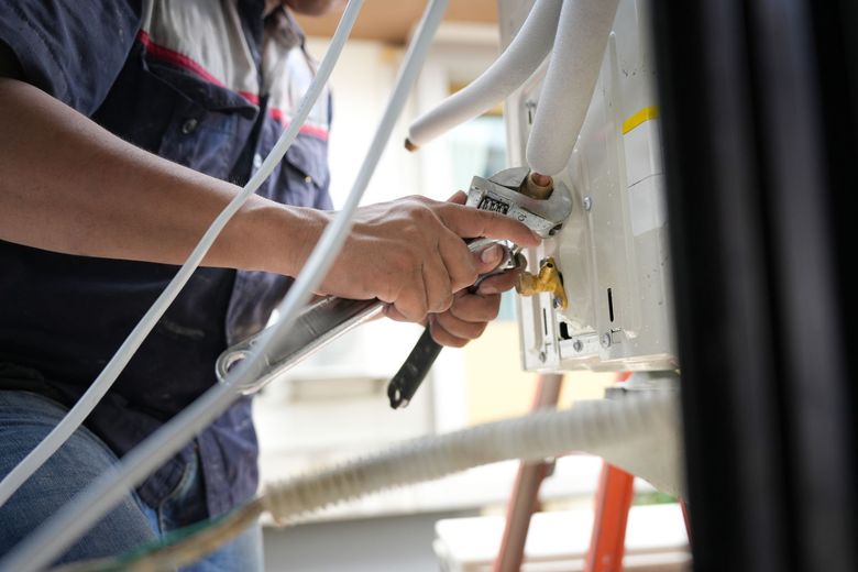 Technician inspecting large silver HVAC ductwork in a bright empty room with a handheld device