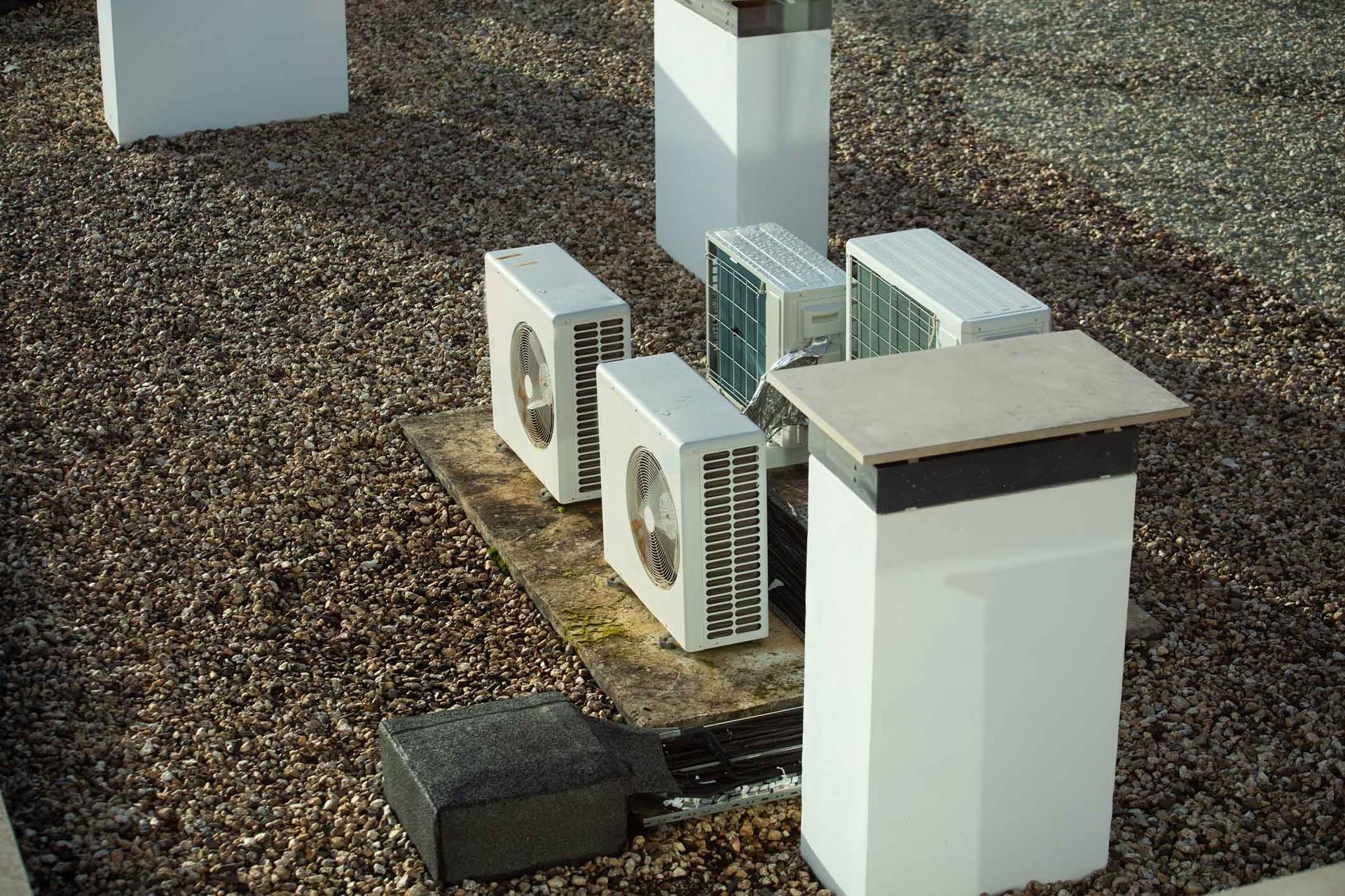 Outdoor HVAC units and electrical boxes on gravel beside a building wall