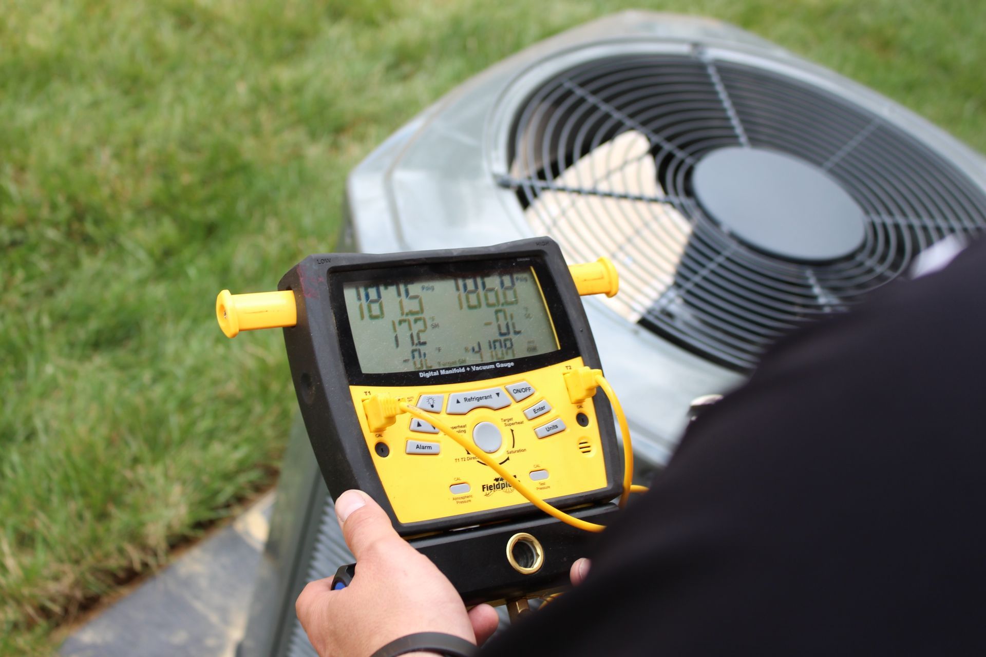Technician in yellow shirt kneeling to inspect wiring on outdoor HVAC unit