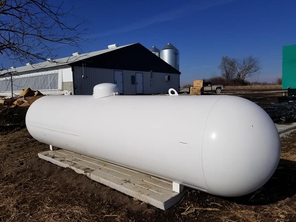 Two large, white horizontal propane storage tanks supported by blue metal stands in an open field under a blue sky.