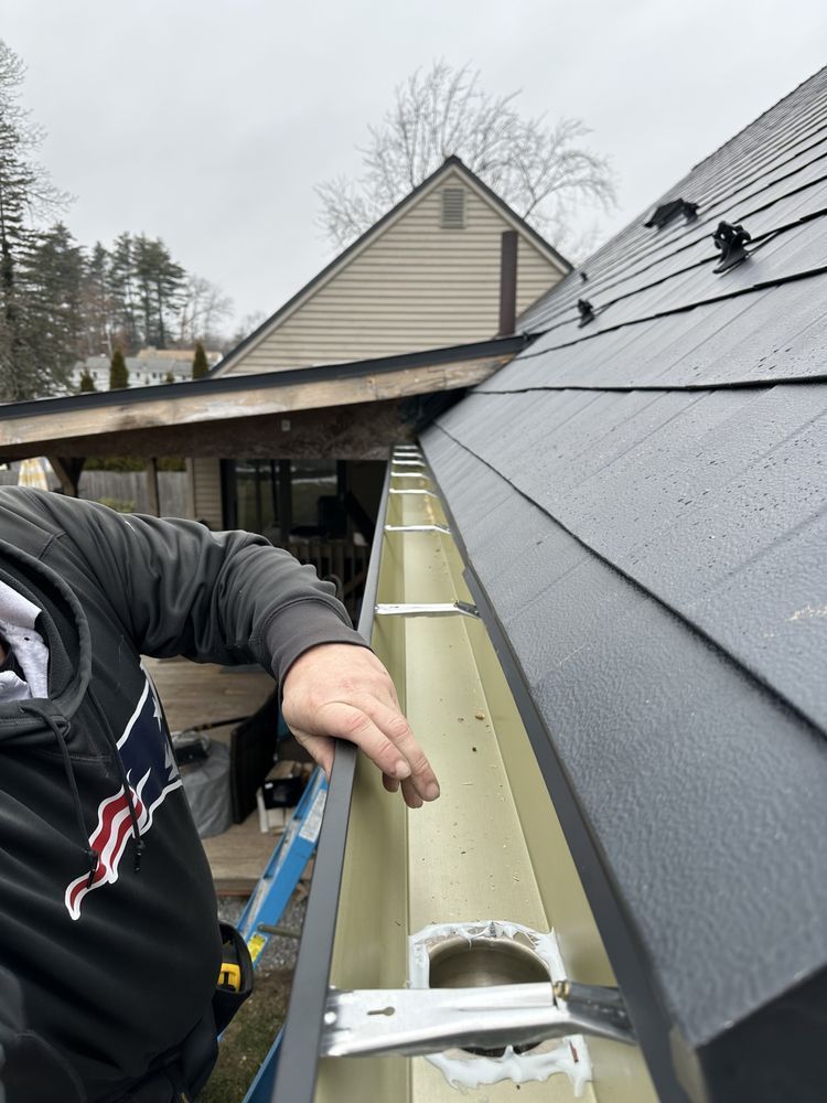 Worker installing gutter on a sloped roof beside a house under construction