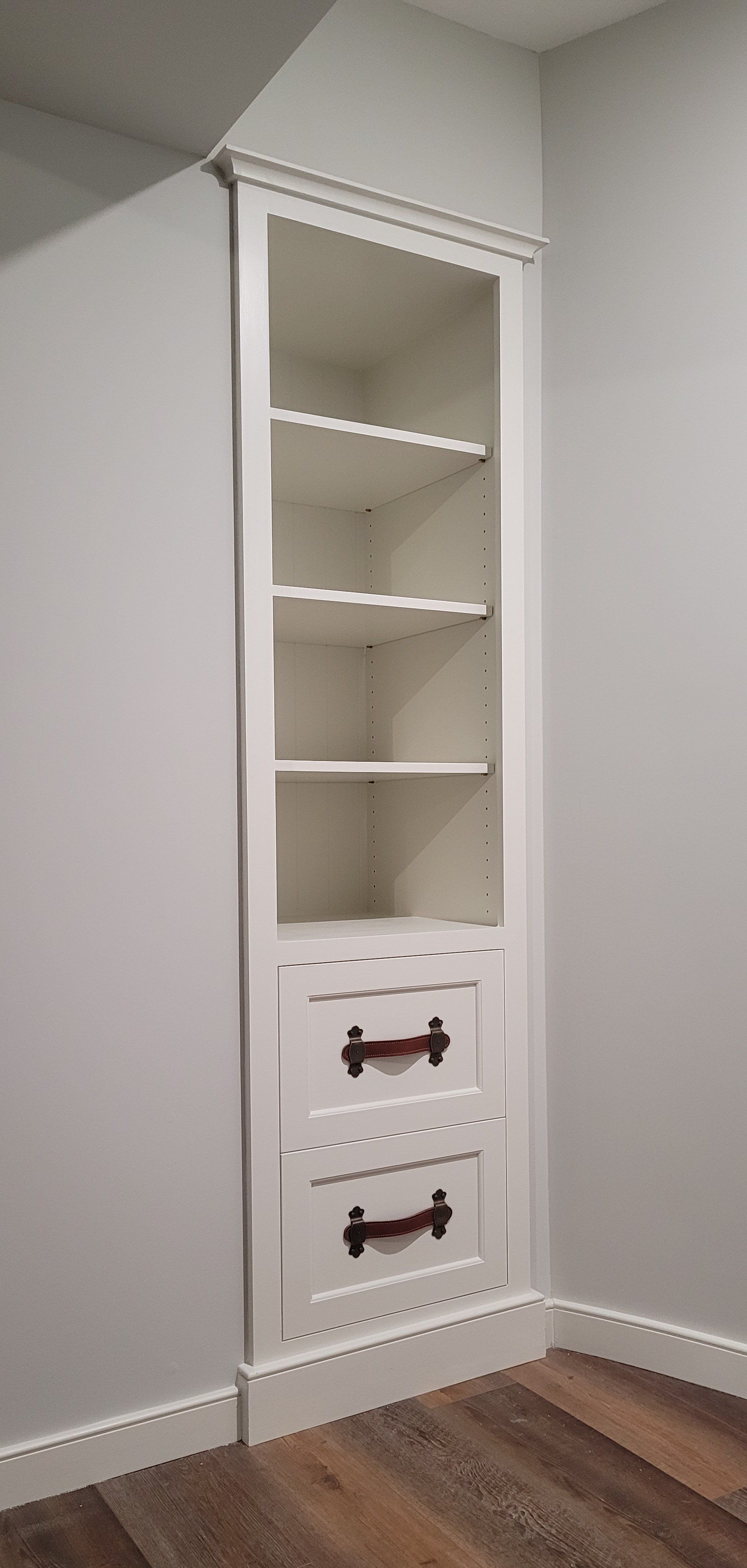 A white bookshelf with two drawers in a corner of a room.