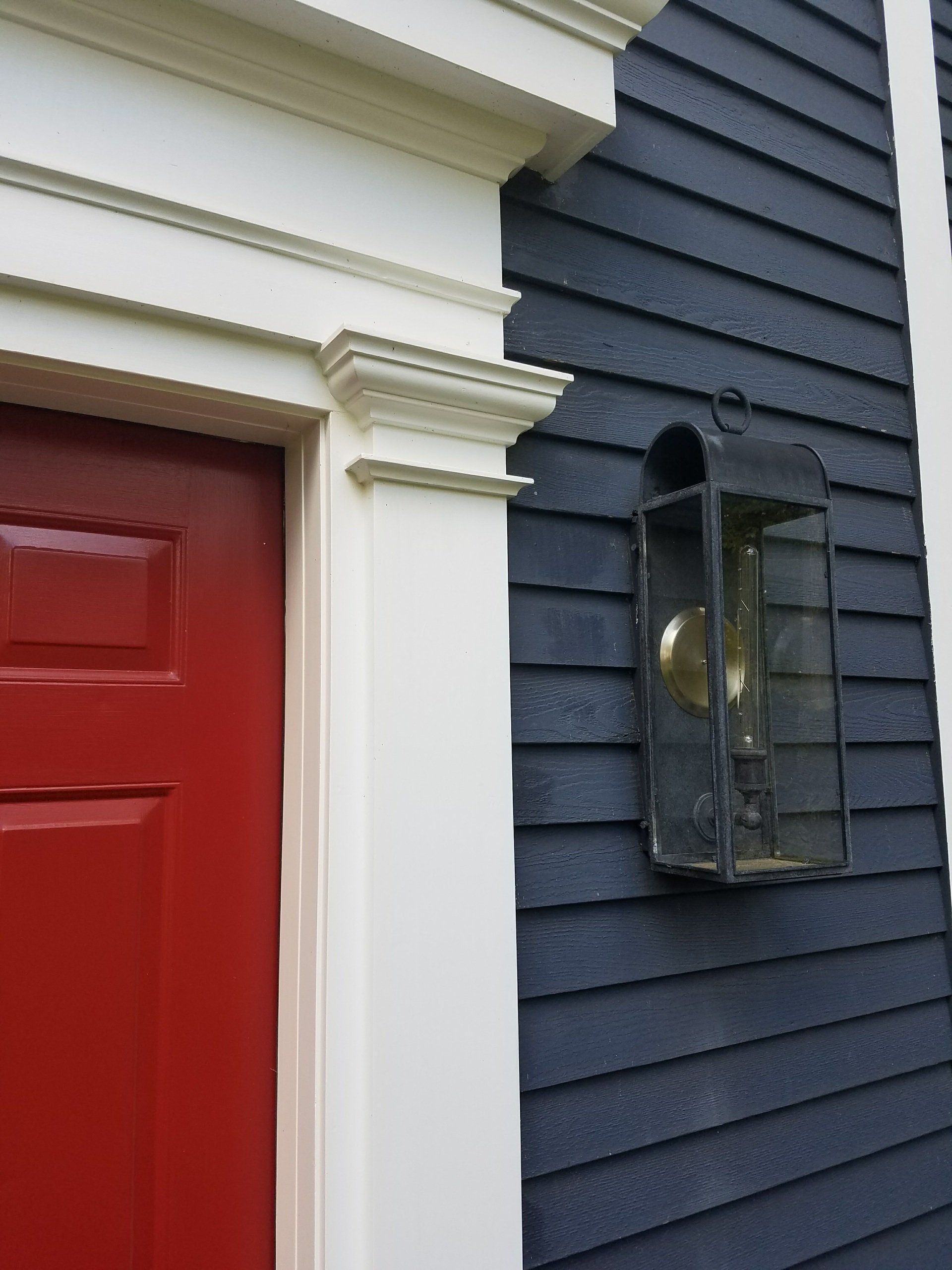 A red door is on the side of a blue house