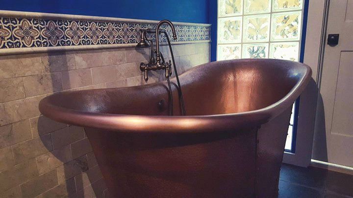 A copper bathtub is sitting in a bathroom next to a window.