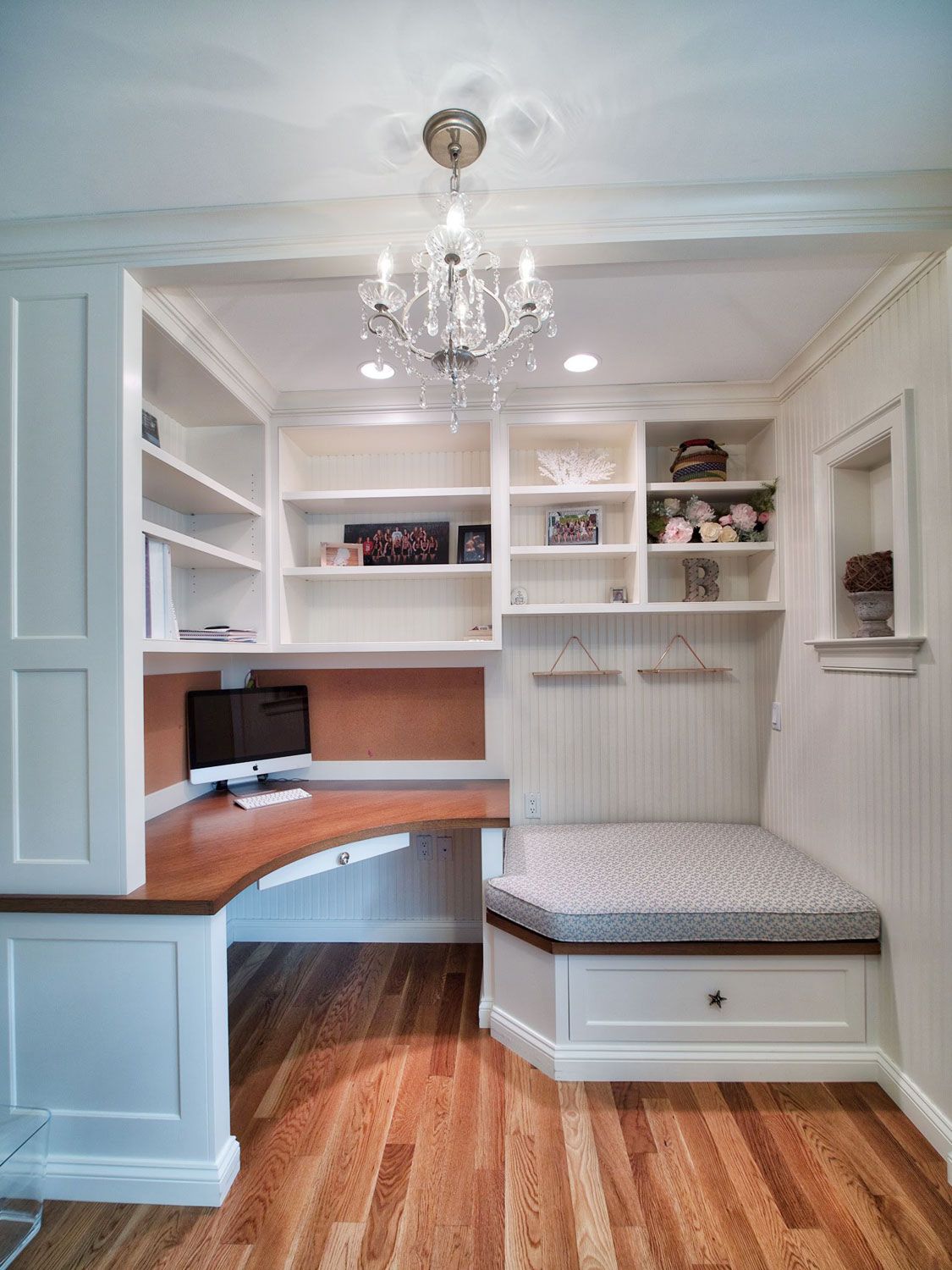 A room with a desk , shelves and a chandelier.