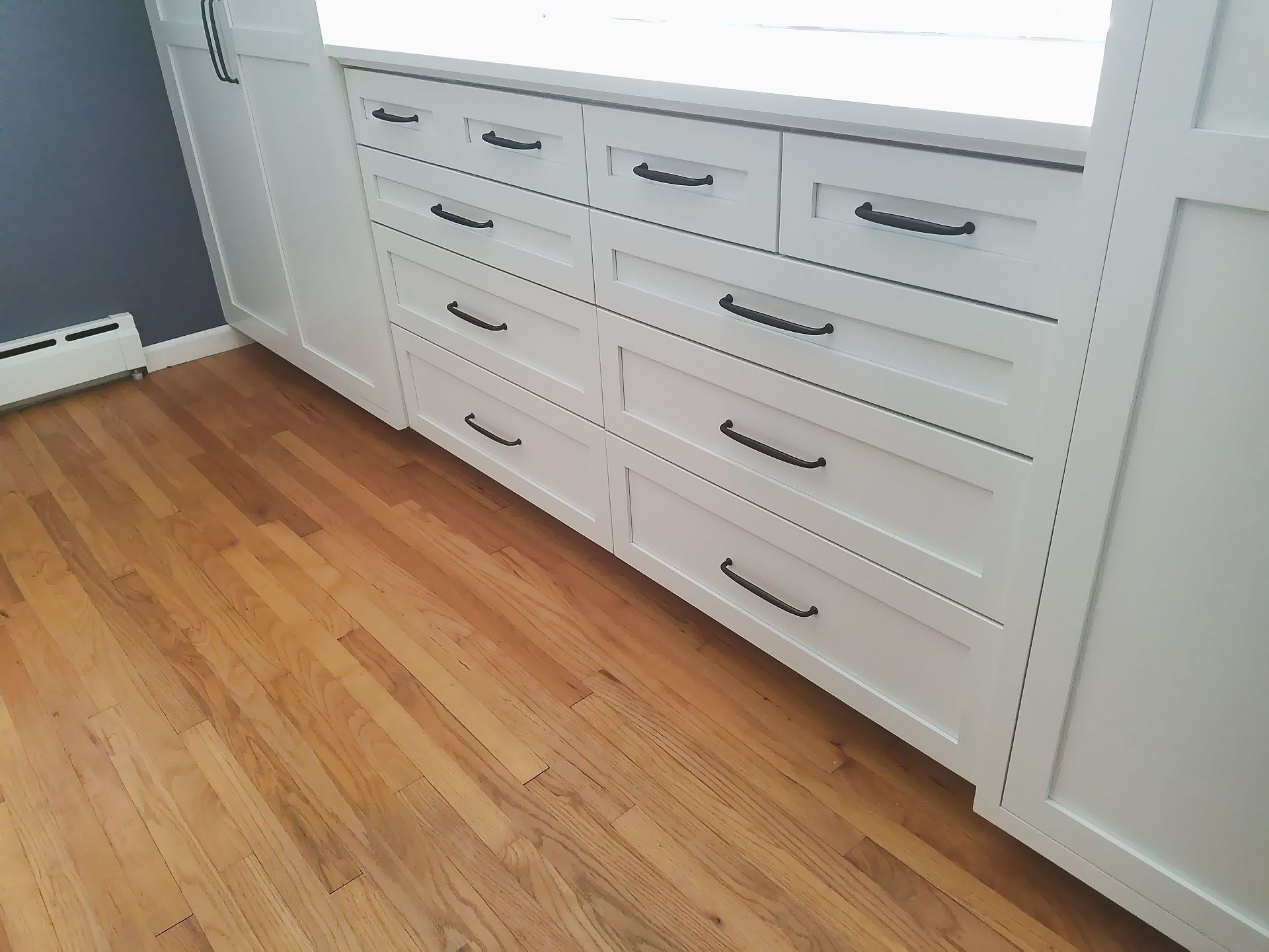 A room with hardwood floors and white cabinets with black handles