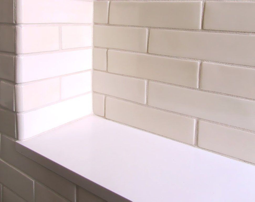 A white brick wall with a white shelf in the corner.