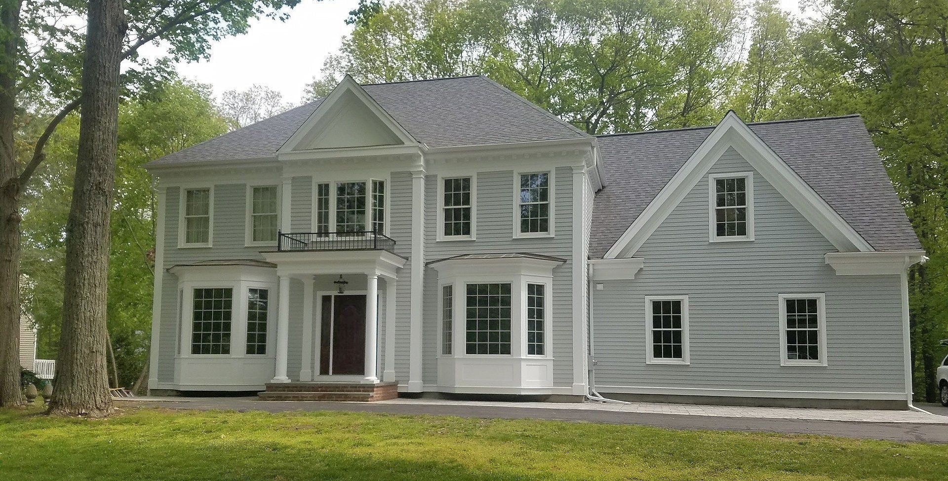 A large white house with a gray roof is surrounded by trees