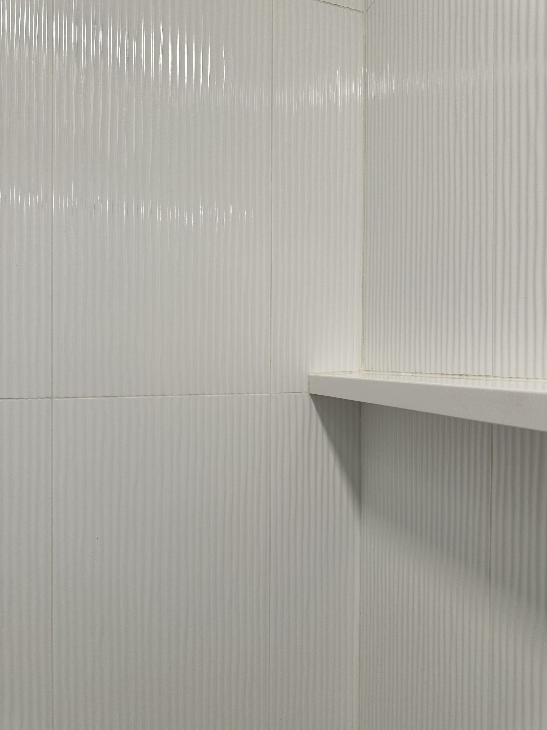 A bathroom with white tiles and a white shelf.