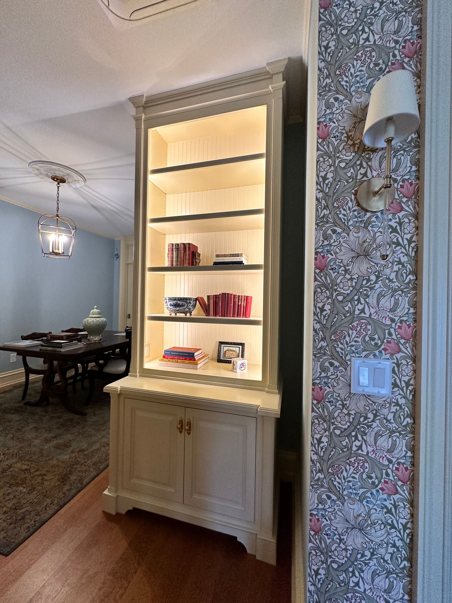 A dining room with a table and chairs and a bookcase with books on it