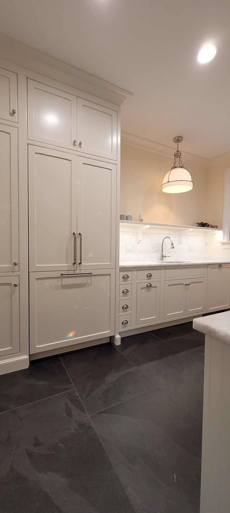 A kitchen with white cabinets and black tile floors.