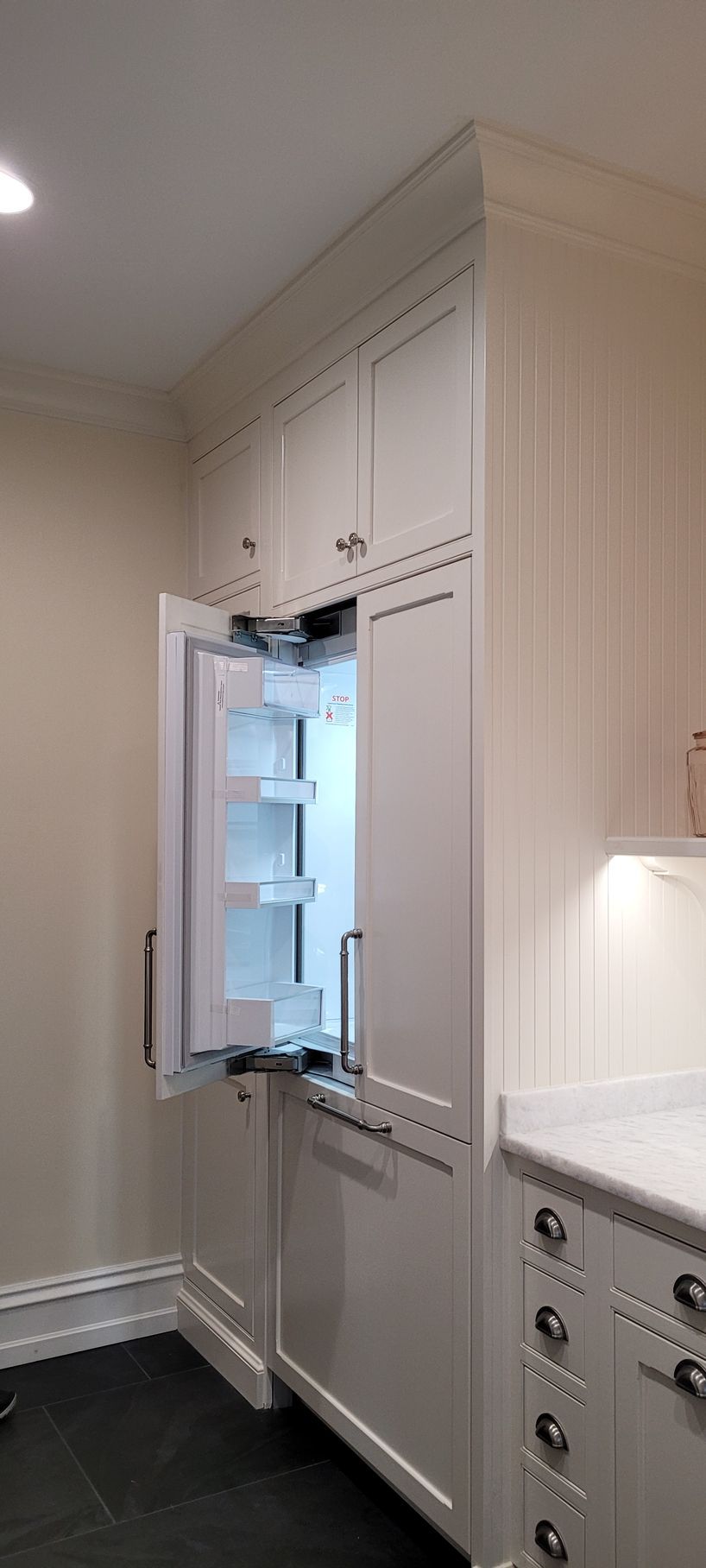 A kitchen with white cabinets and a refrigerator with the door open.