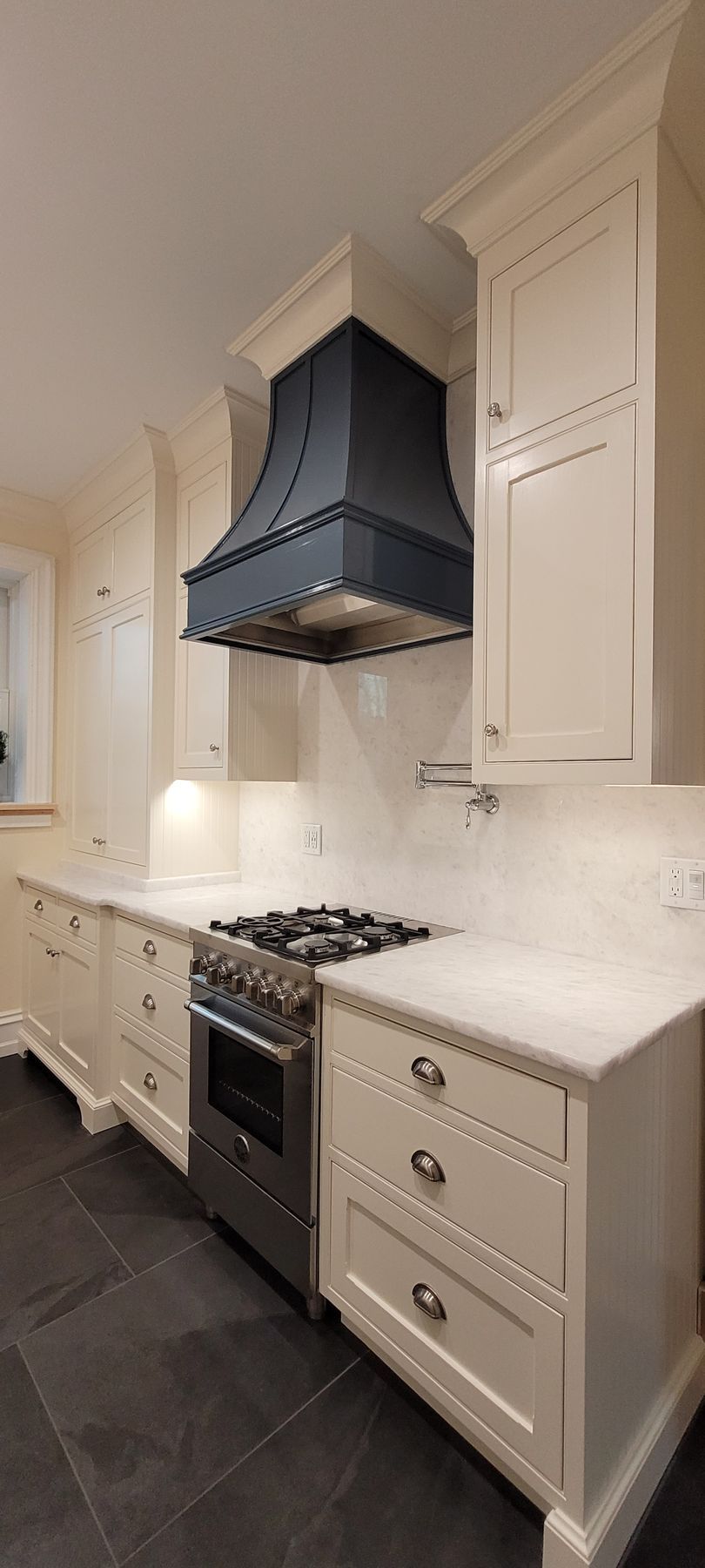 A kitchen with white cabinets , a stove , and a blue hood.
