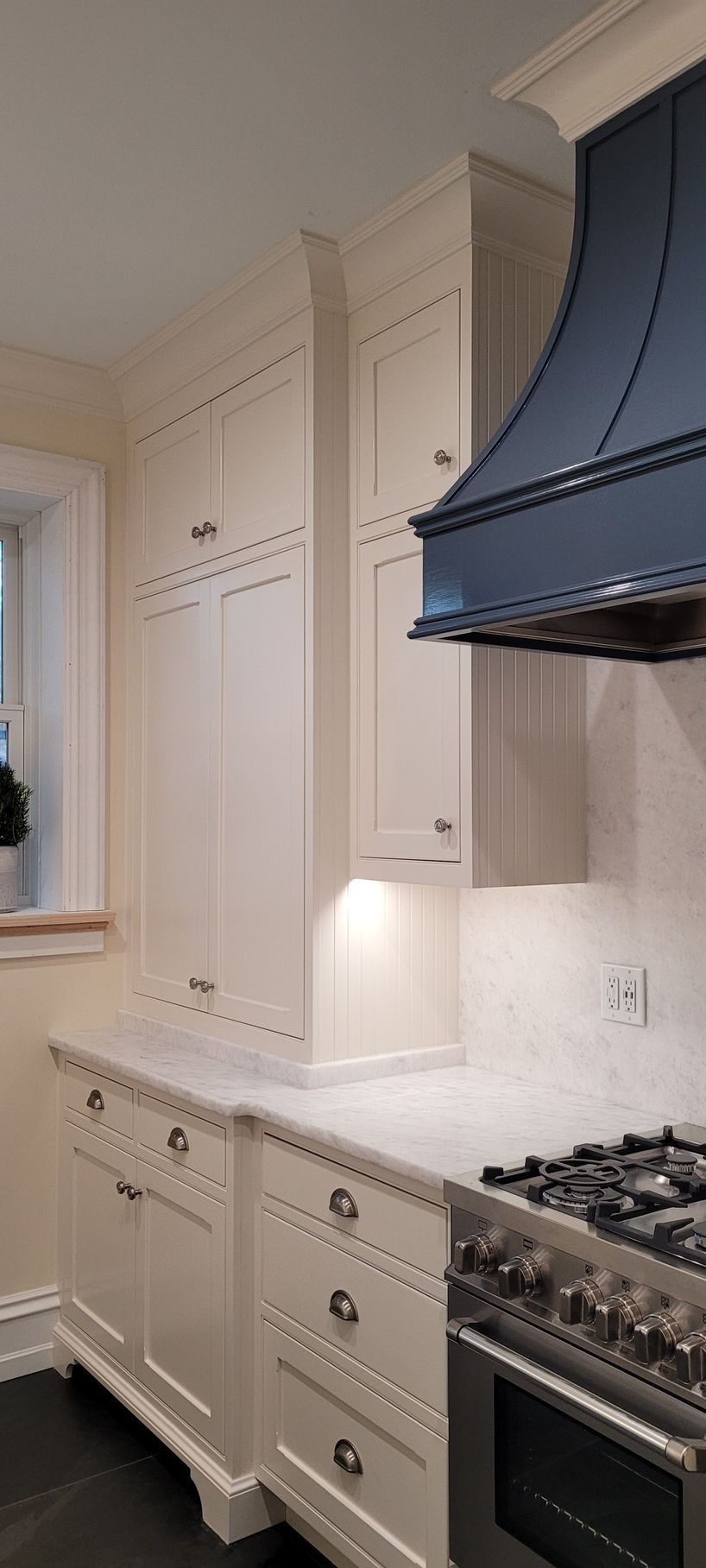 A kitchen with white cabinets , a stove , and a blue hood.