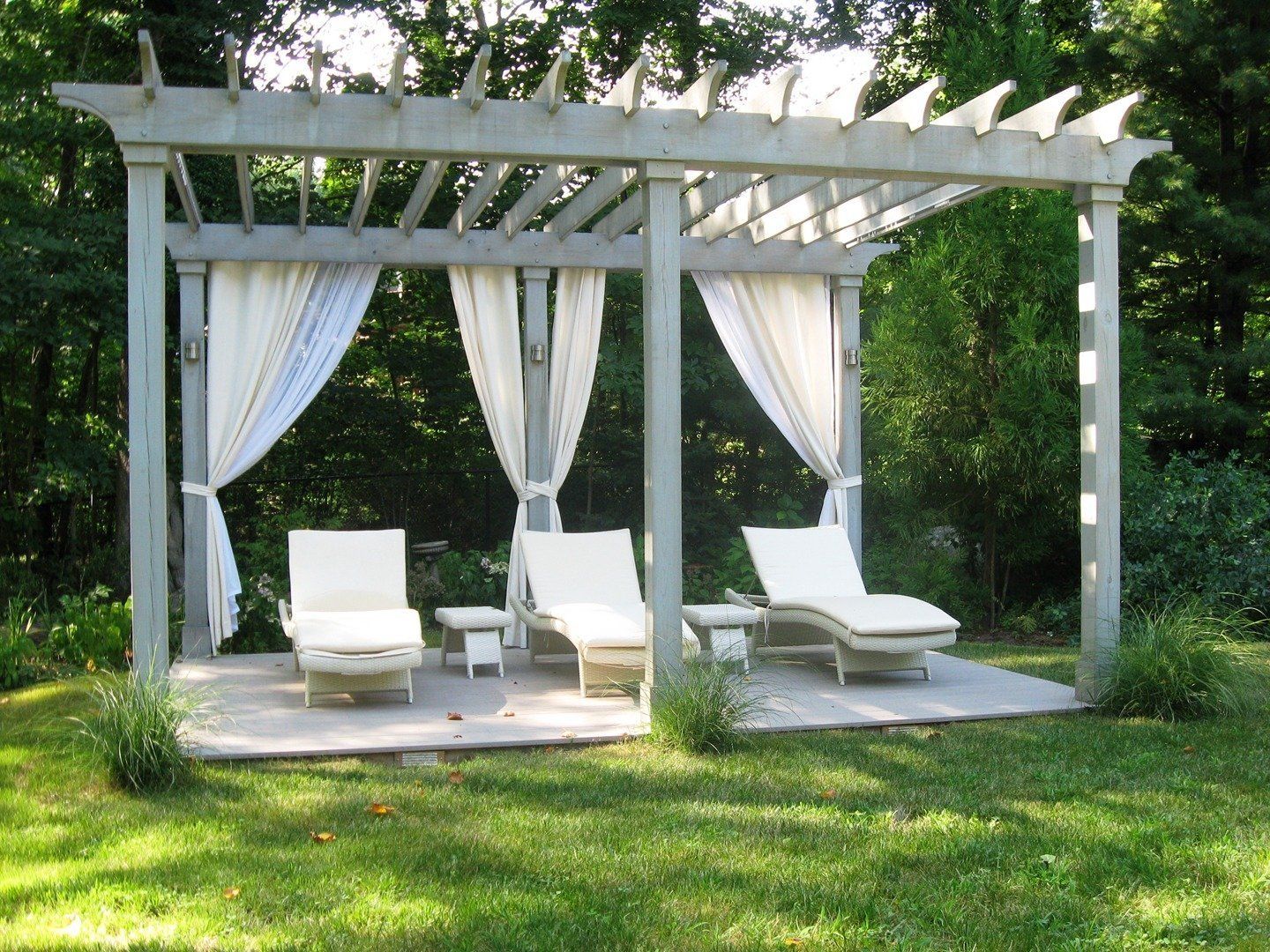 Two lounge chairs under a pergola with white curtains
