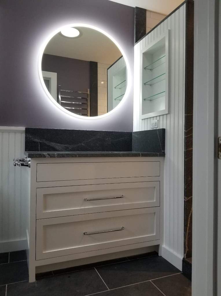 A bathroom with a round mirror and a dresser.