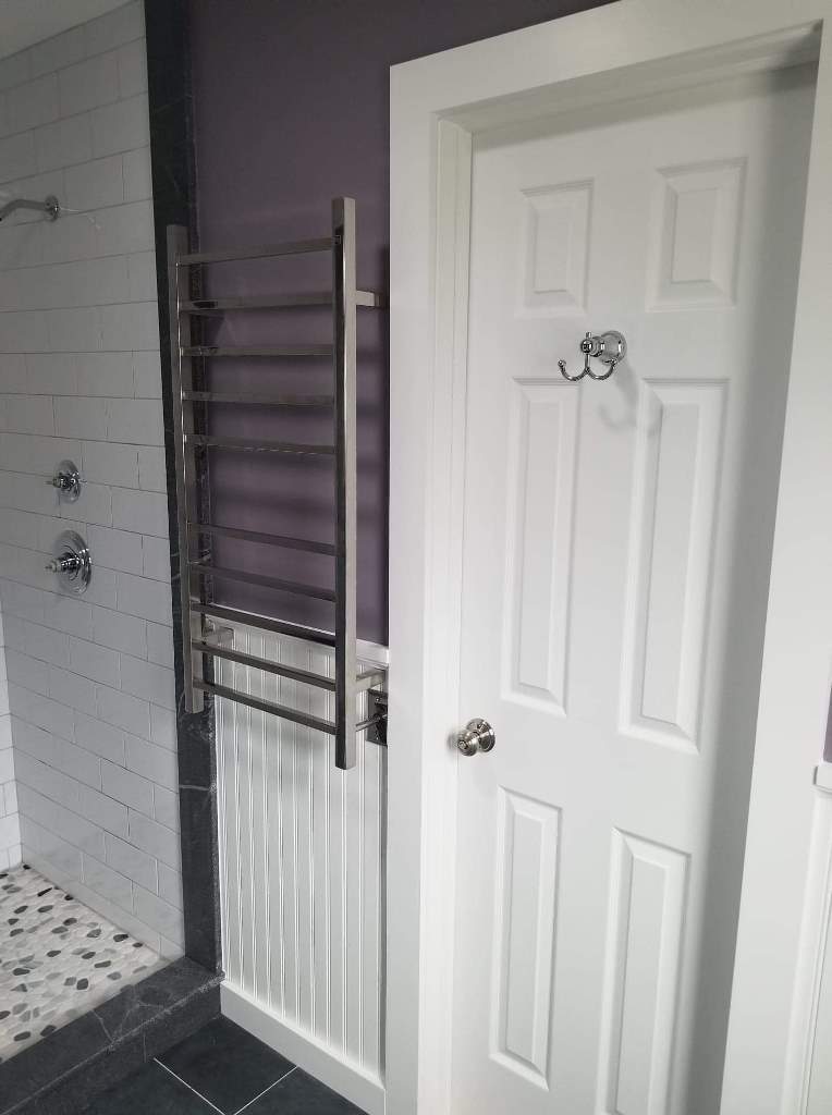 A bathroom with a white door and a towel rack on the wall.