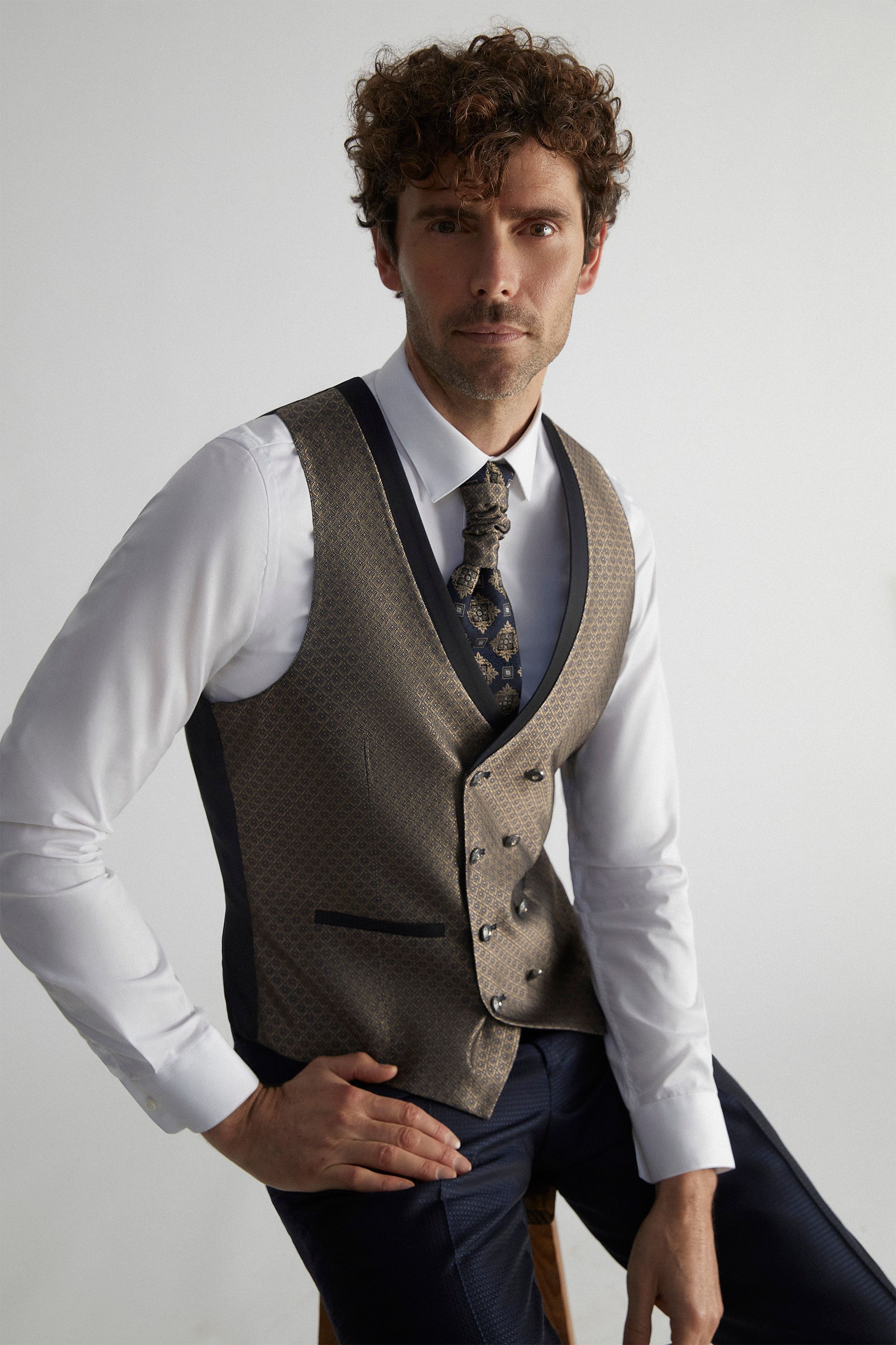 Un uomo che indossa un gilet e una cravatta è seduto su uno sgabello.