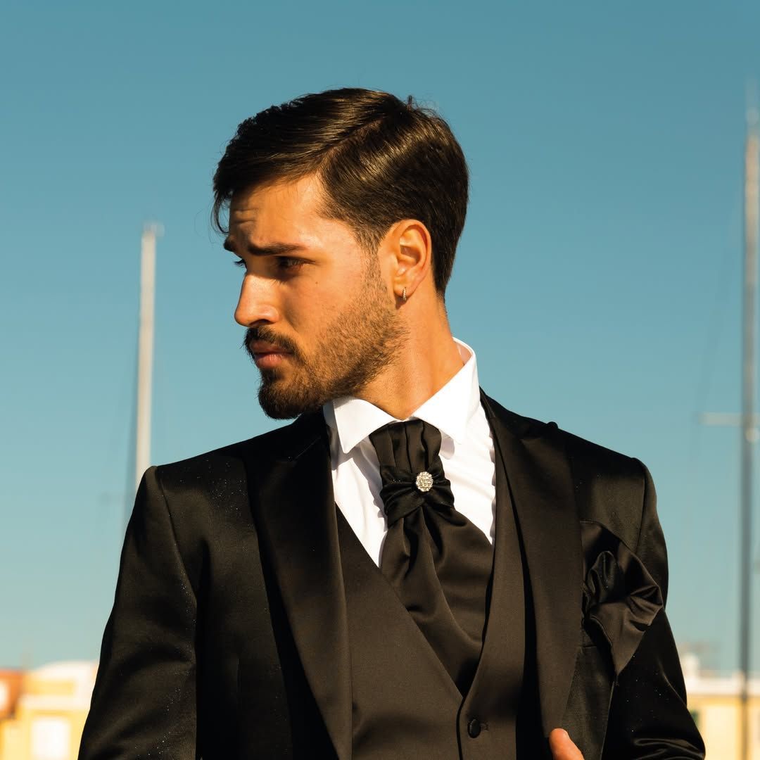 Un uomo in abito nero e cravatta è in piedi davanti a un cielo azzurro