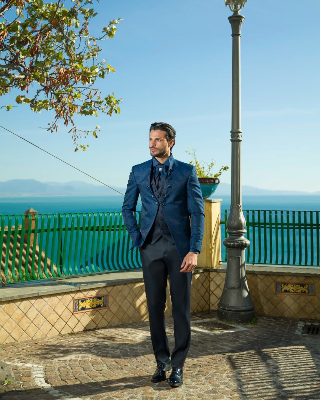 Un uomo in abito blu è in piedi davanti a una recinzione che si affaccia sull'oceano.