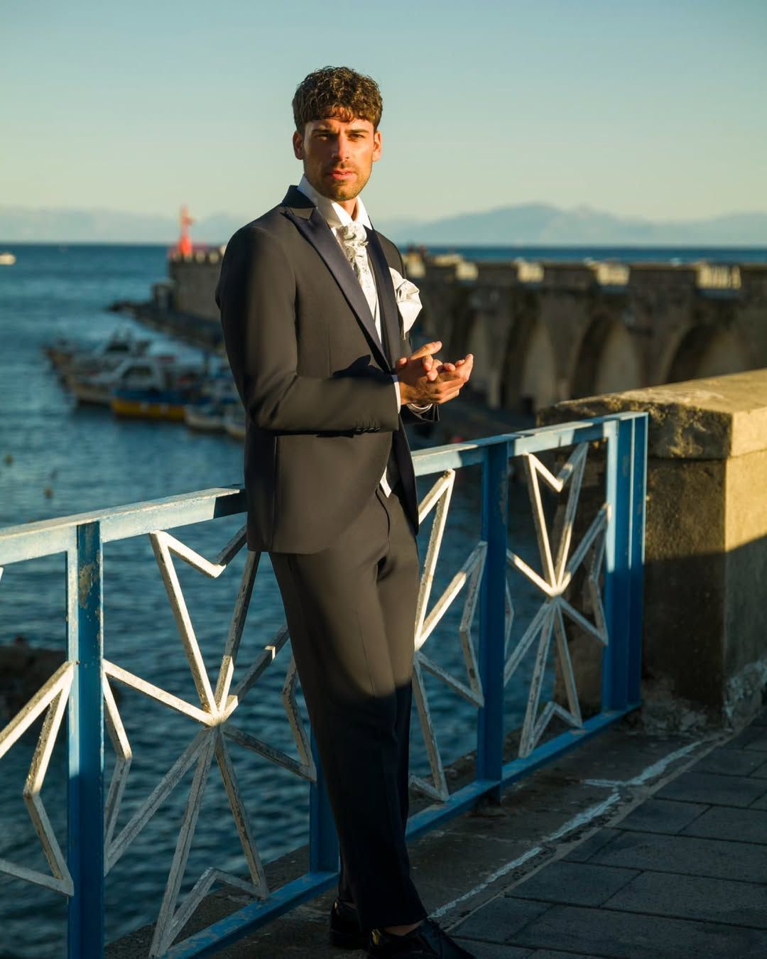 Un uomo in giacca e cravatta è appoggiato a una ringhiera che si affaccia sull'oceano.