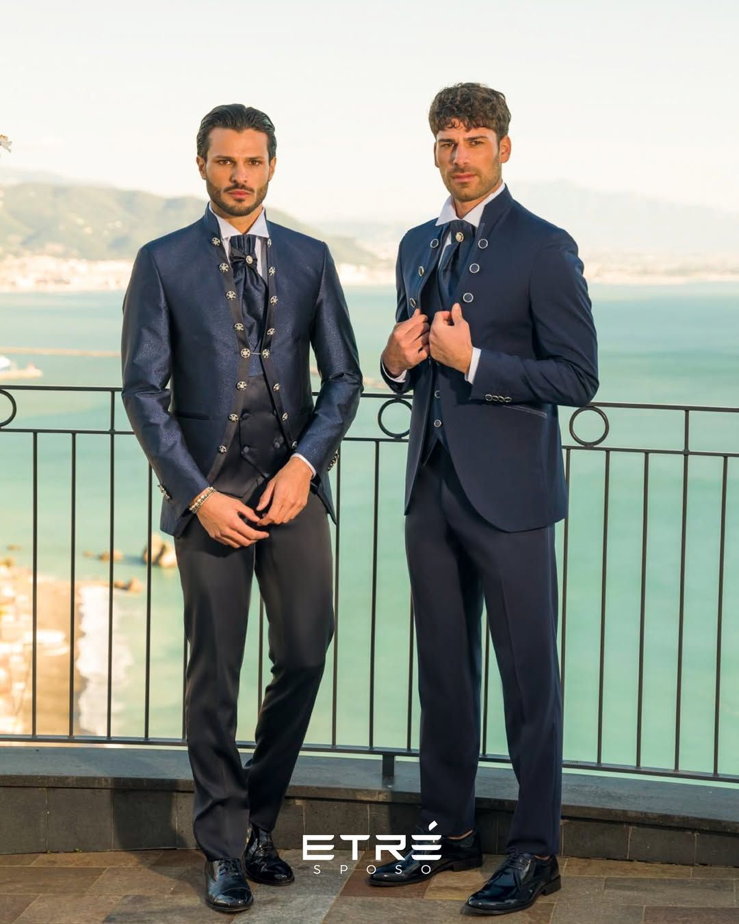 Due uomini in giacca e cravatta sono in piedi uno accanto all'altro su un balcone che si affaccia sull'oceano.