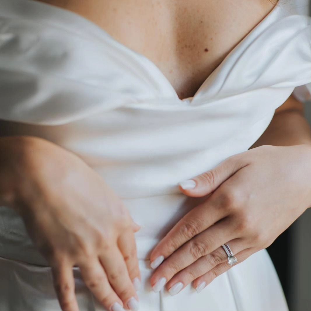 Una donna vestita di bianco tiene le mani sullo stomaco.