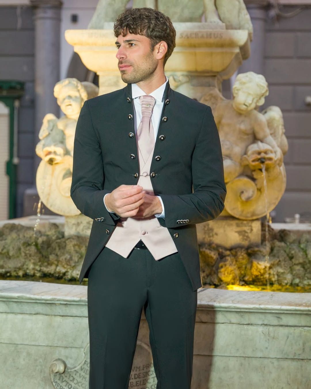 Un uomo in giacca e cravatta è in piedi davanti a una fontana.