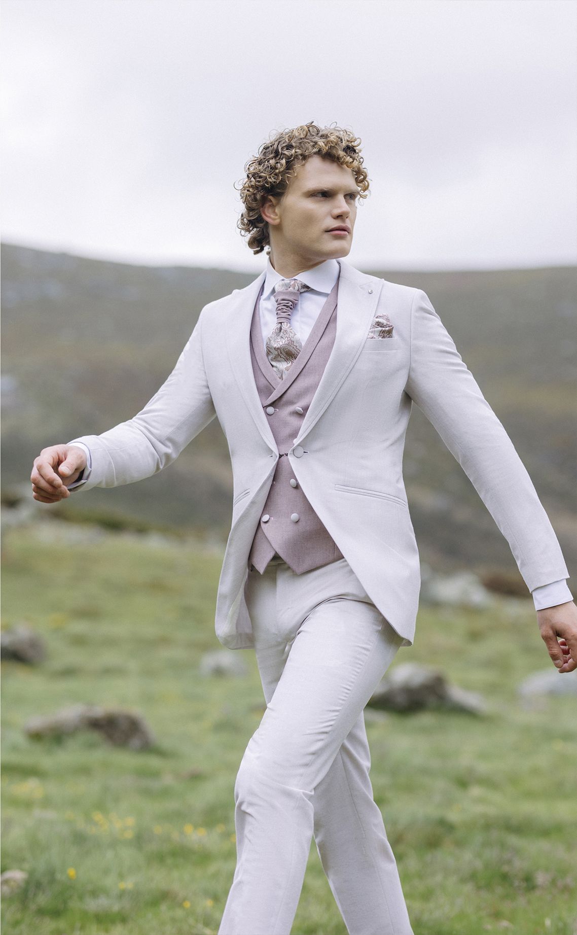 Un uomo in abito bianco e cravatta sta camminando in un campo.