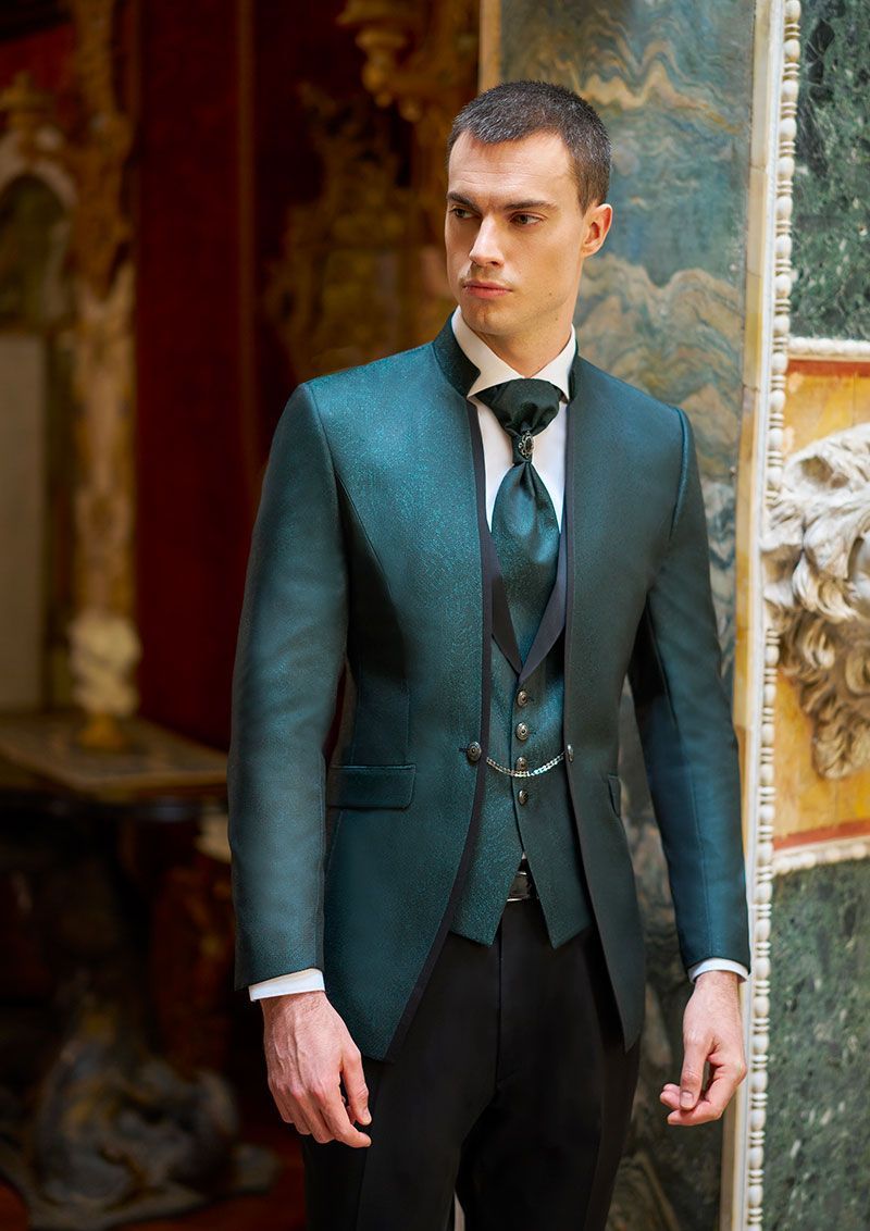 Un uomo in giacca e cravatta verde è in piedi in una stanza.