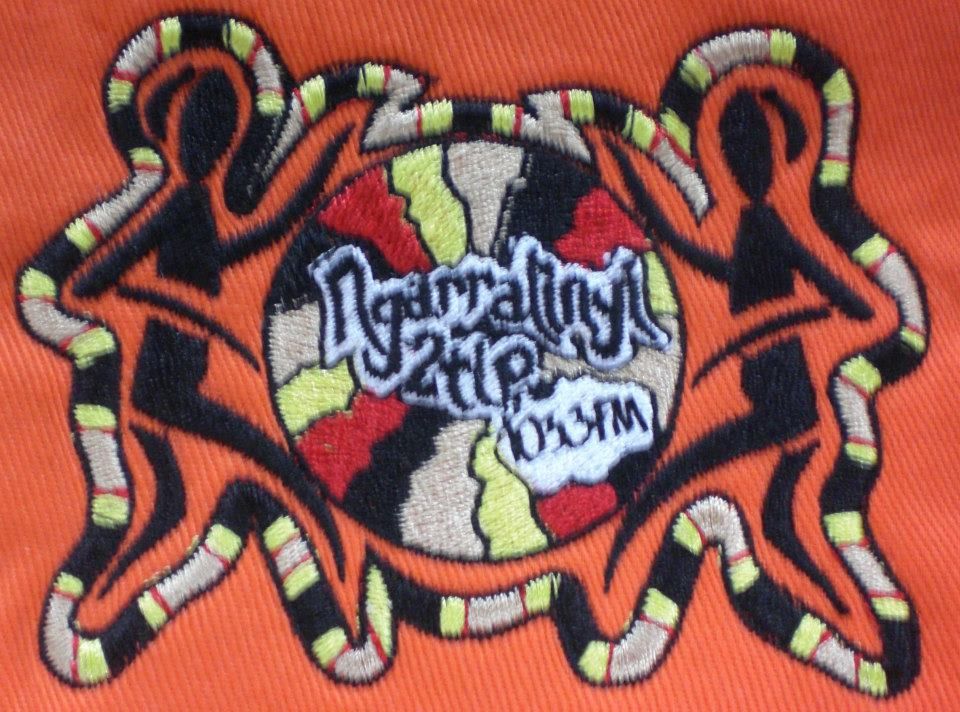Embroidered patch with tribal figures flanking a colourful central design on orange fabric — Workwise Clothing Forster in Forster, NSW
