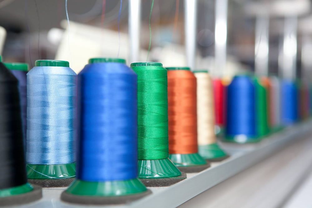 Spools of Colorful Thread Lined Up on a Shelf, Ready for Sewing or Embroidery — Workwise Clothing Forster in Forster, NSW
