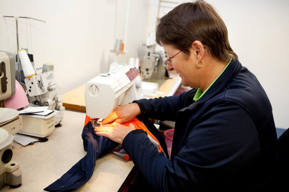 Woman Sewing With a Machine at a Table — Workwise Clothing Forster in Forster, NSW