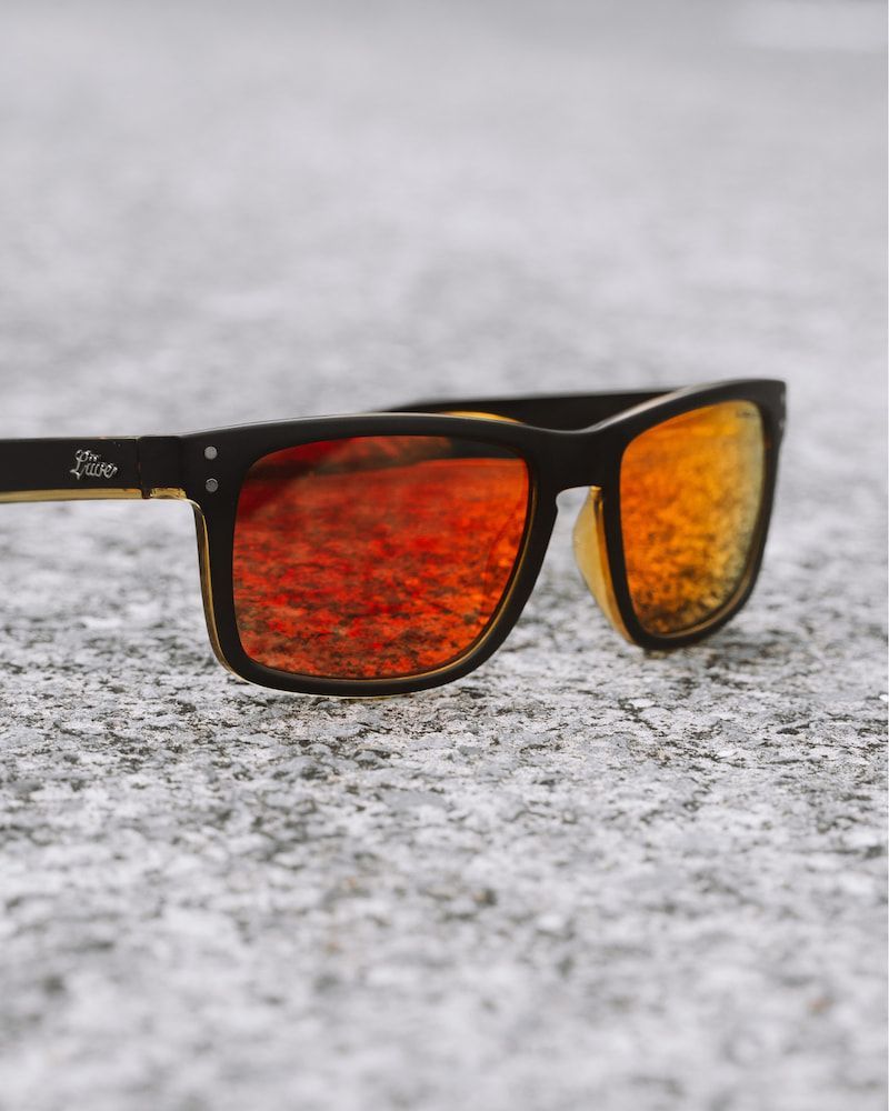 Black Sunglasses With Orange-red Mirrored Lenses Resting on a Speckled — Workwise Clothing Forster in Forster, NSW