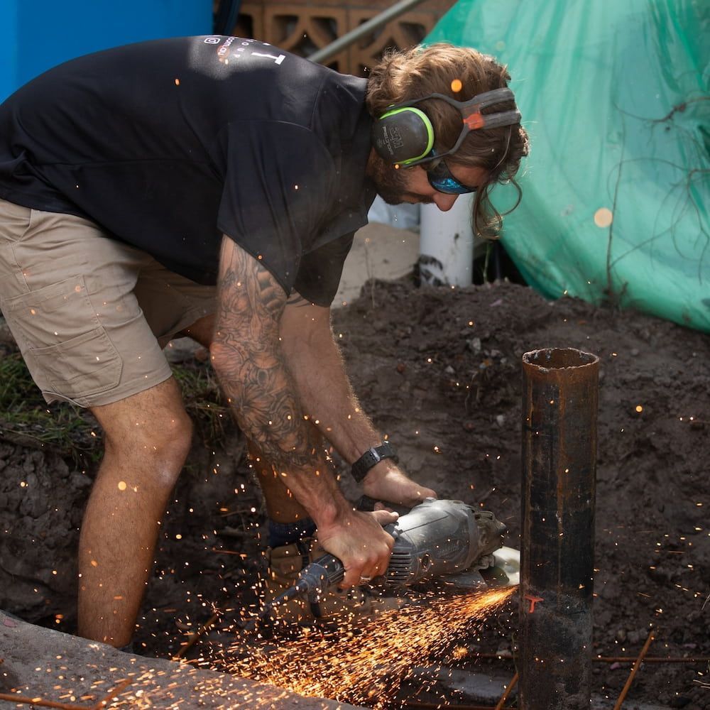 Man in Shorts Uses a Grinder on a Metal Post, Outdoors — Workwise Clothing Forster in Forster, NSW