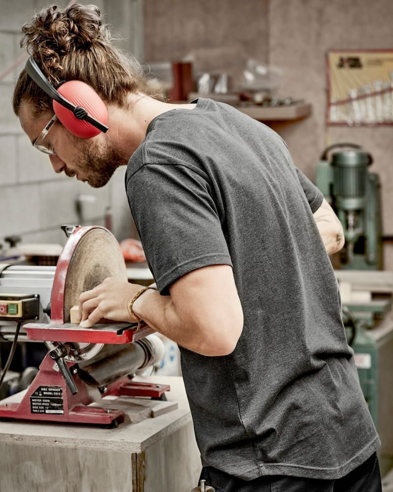 Man With Ear Protection Sanding Wood Disc in Workshop — Workwise Clothing Forster in Taree, NSW