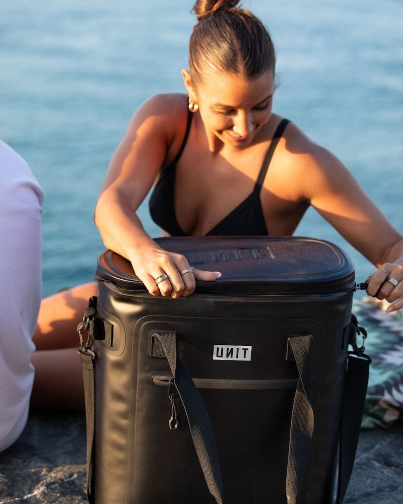 Woman in a Black Bikini Opening a Black Unit Cooler by the Ocean — Workwise Clothing Forster in Forster, NSW
