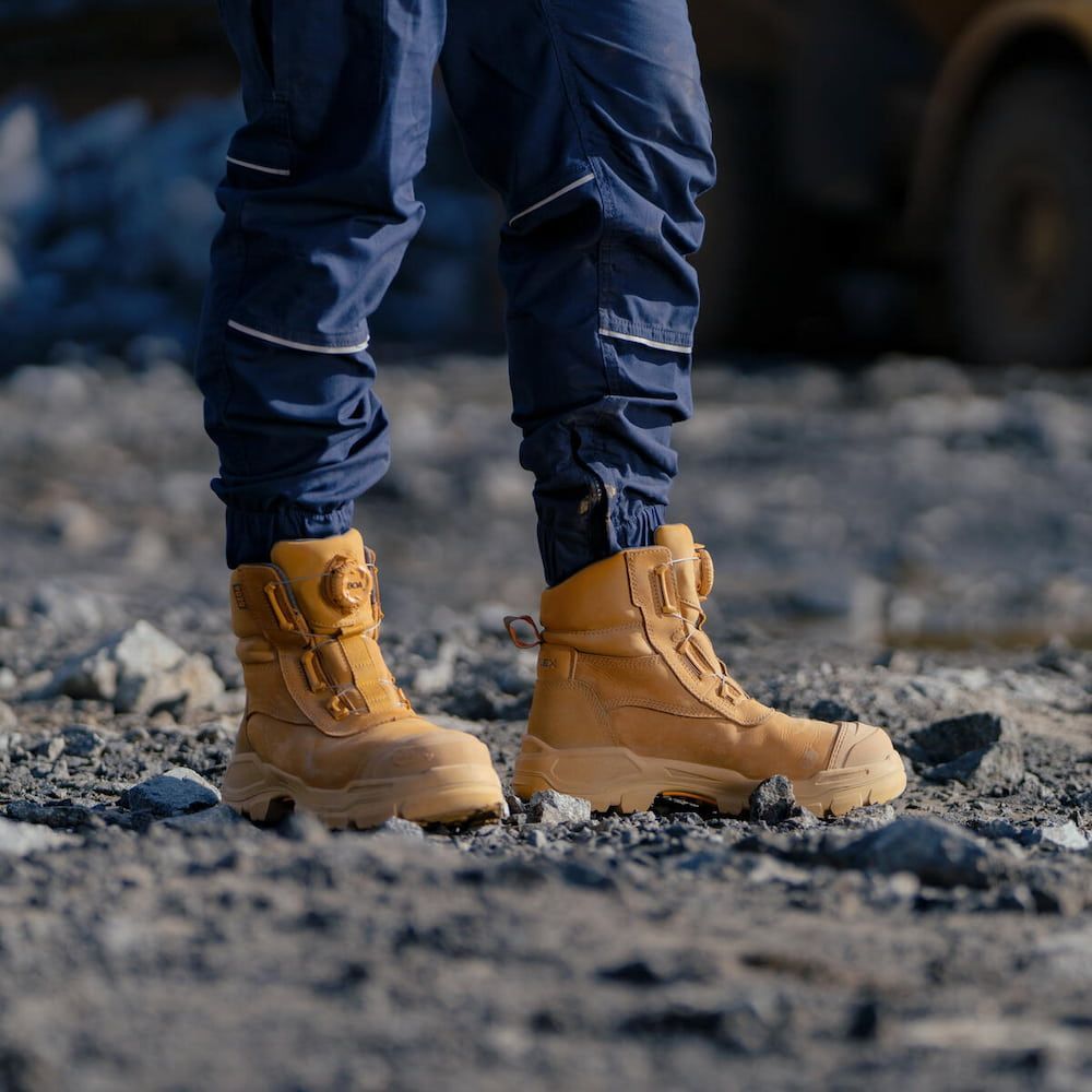 Person in Tan Work Boots and Blue Pants Standing on Rocky Ground — Workwise Clothing Forster in Forster, NSW