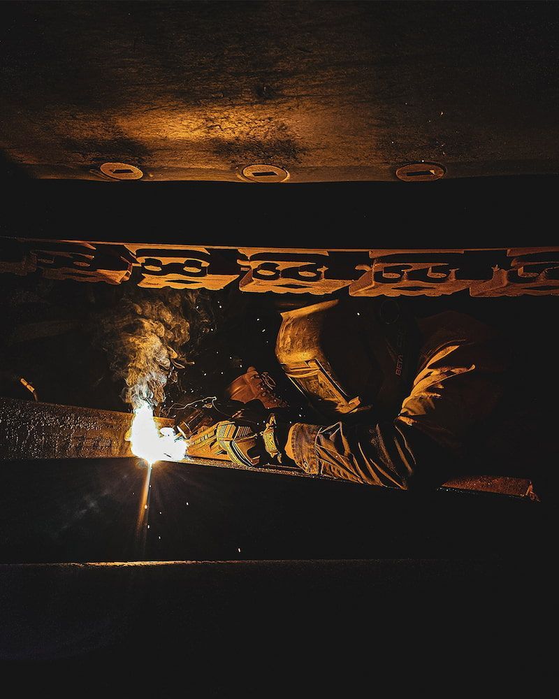 Welder in Dark Setting, Sparks Flying as They Work on Metal — Workwise Clothing Forster in Forster, NSW