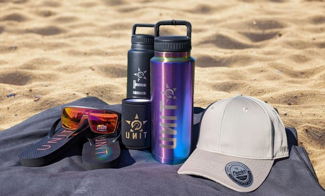 Beach Scene With Water Bottles, Sunglasses, a Cap, and a Towel on the Sand — Workwise Clothing Forster in Forster, NSW