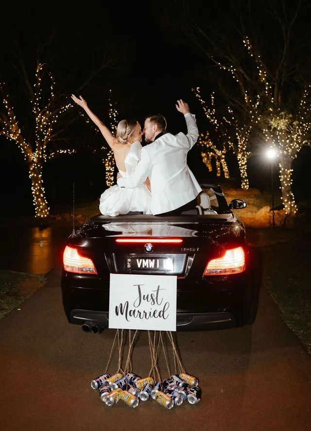 A bride and groom are sitting in the back of a car with a just married sign.
