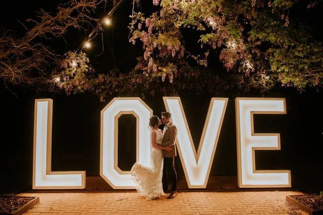 A bride and groom are standing in front of a large love sign.
