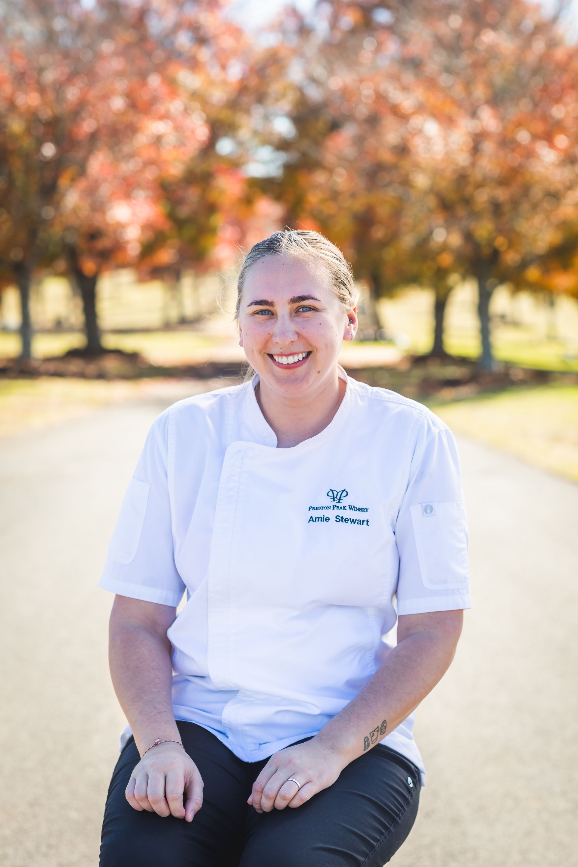 A woman in a white chef 's coat is sitting on the side of a road.