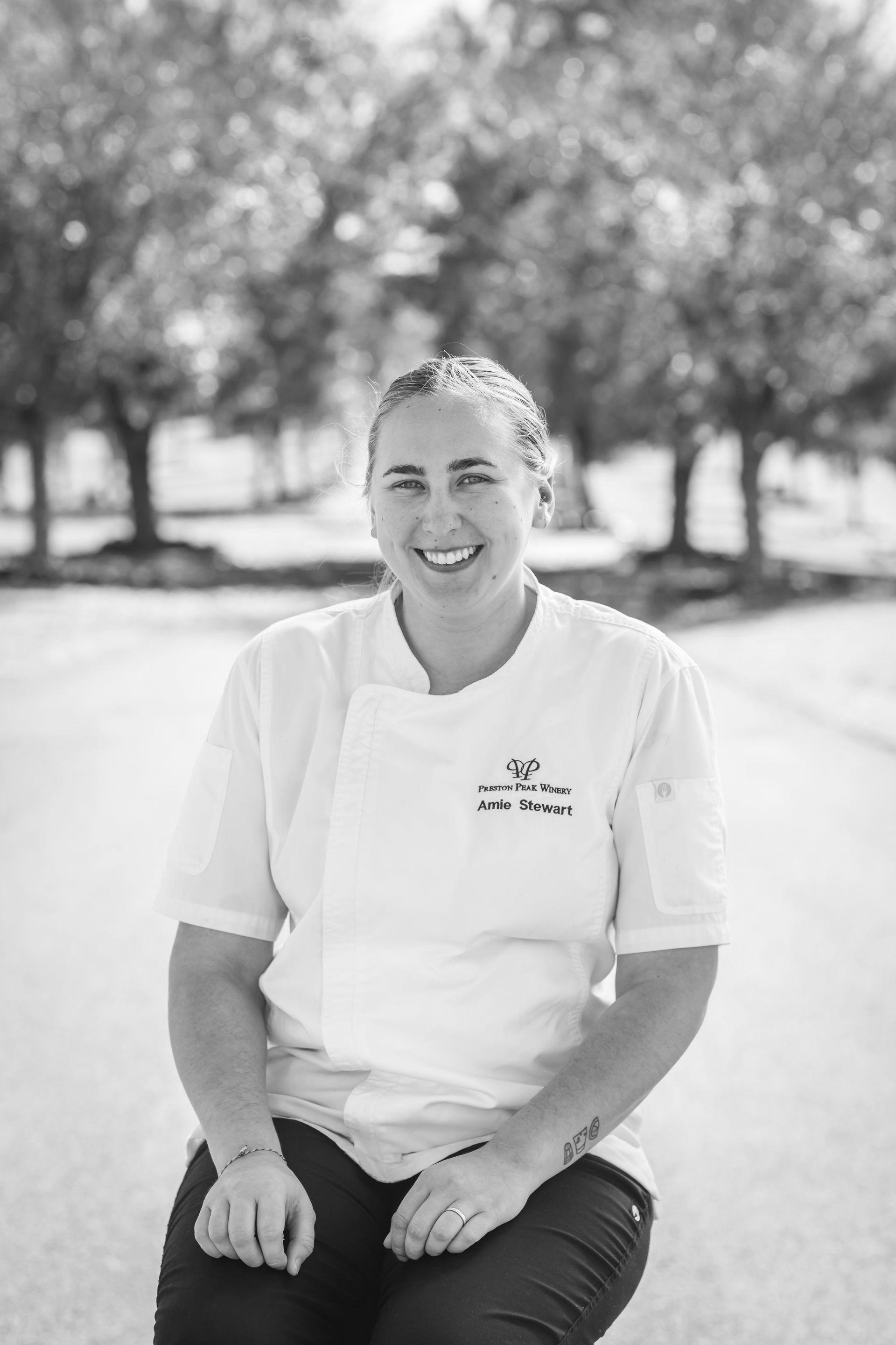 A black and white photo of a woman in a chef 's coat sitting on a bench.