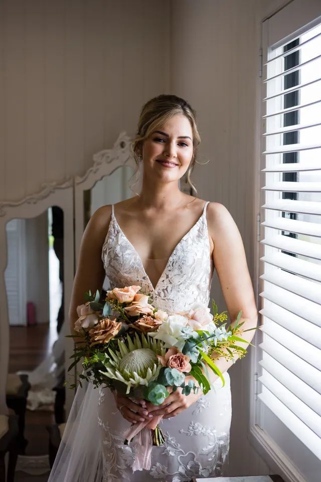 A bride in a wedding dress is holding a bouquet of flowers in front of a window.