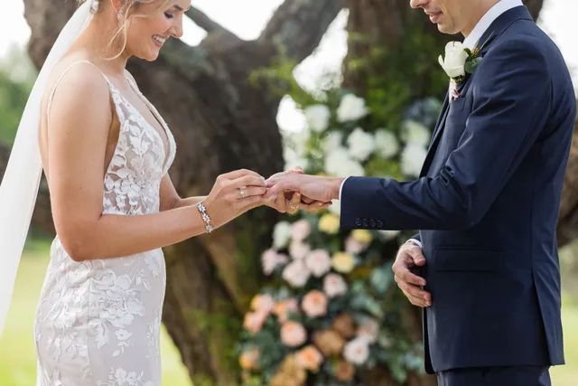 A bride and groom are putting a wedding ring on each other 's finger.