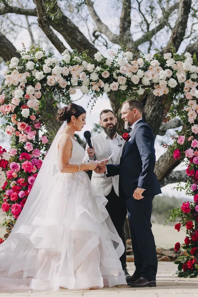 A bride and groom are getting married under a tree with flowers.